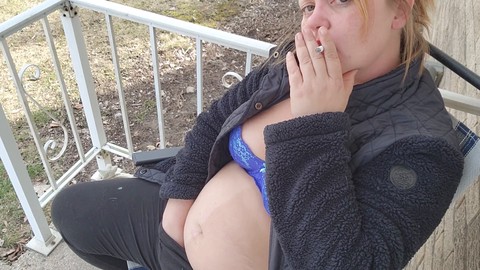 Una chica ardiente disfruta de un cigarrillo mientras se complace al aire libre